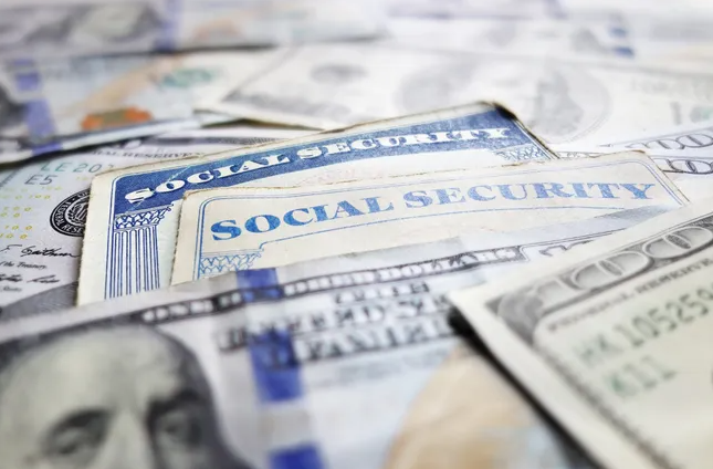Social Security Cards tucked between scattered U.S currency. Getty Image